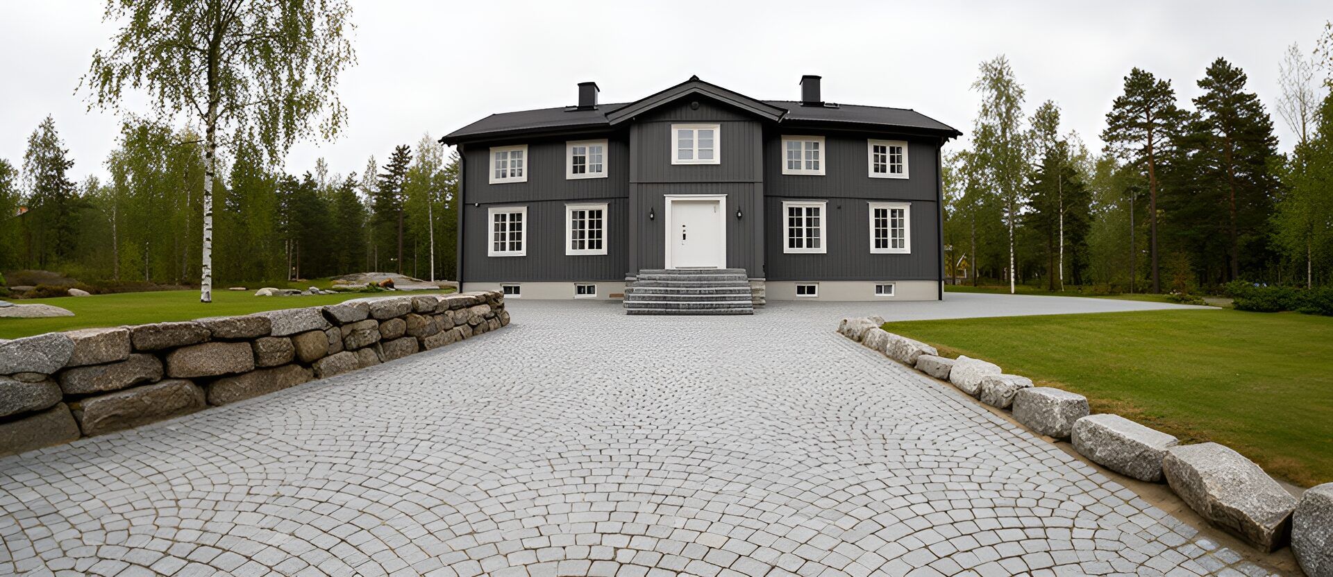Uppfart i grå gatsten lagd i solfjäder fram till en mörkgrå trävilla